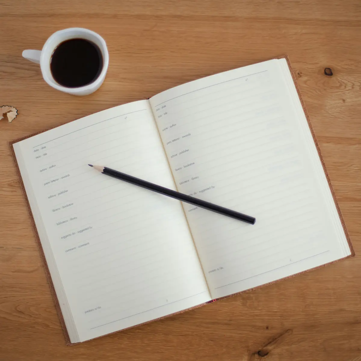 Open notebook with a pencil resting on it, and a cup of coffee next to it.