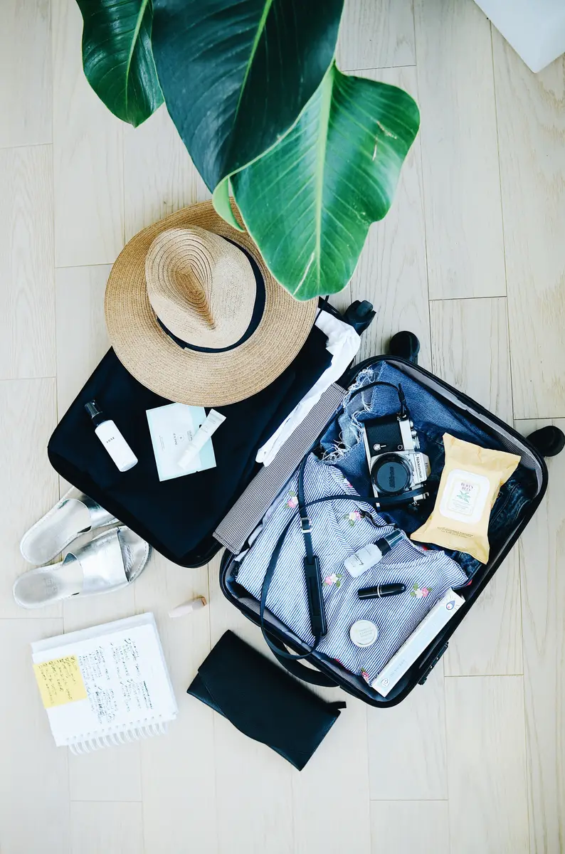 Half packed luggage with a camera, hat, chargers, notebook, and more. 