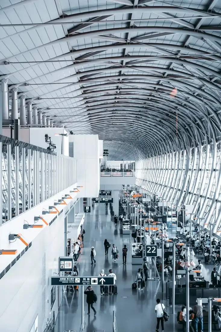 Interior of an airport, with ribbed ceiling, people walking with luggage.