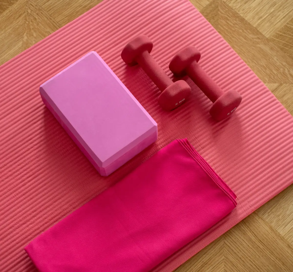 Pink yoga mat with pink block, dumbbells, and towel on the mat. 