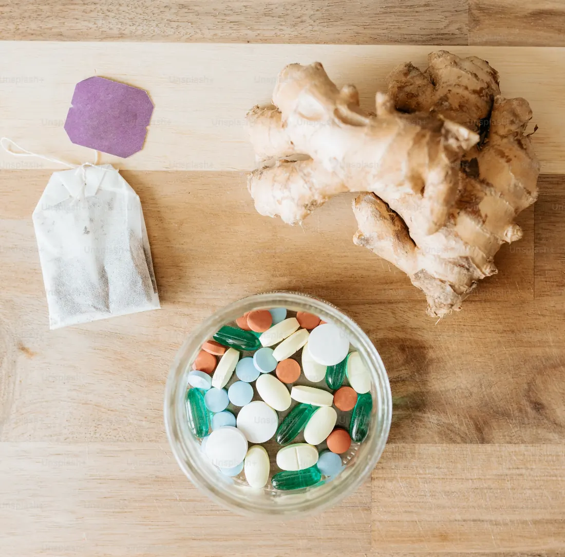 A tea bag, ginger, and a bowl of colorful mixed pills. 