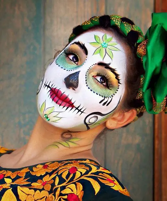 Woman with dark hai, dressed in traditional clothes, with her face painted like a skull, with orange and green details. 