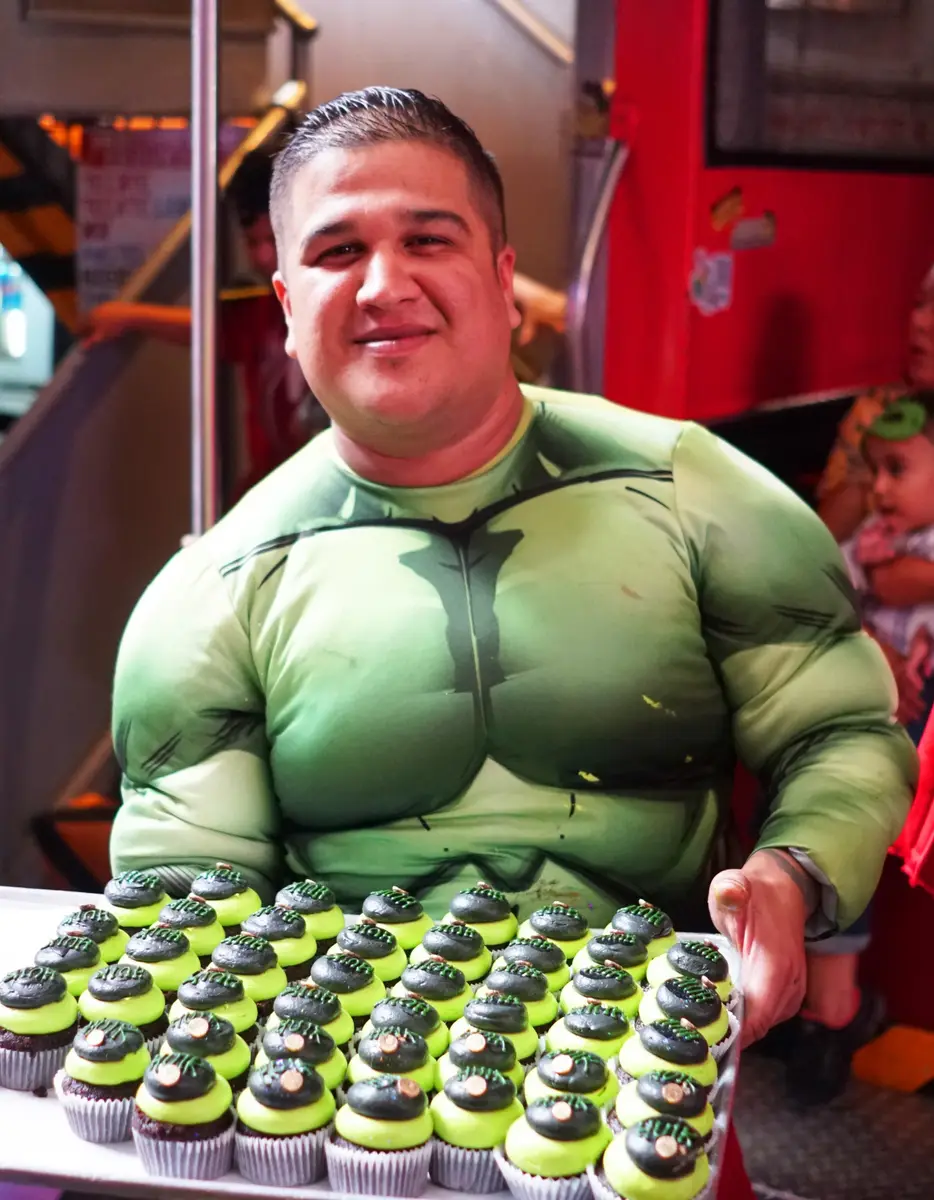 Server from El Squid ROe dressed up as the Hulk holding a tray of superhero themed cupcakes at their Children's Day event in Cabo, Mexico. 