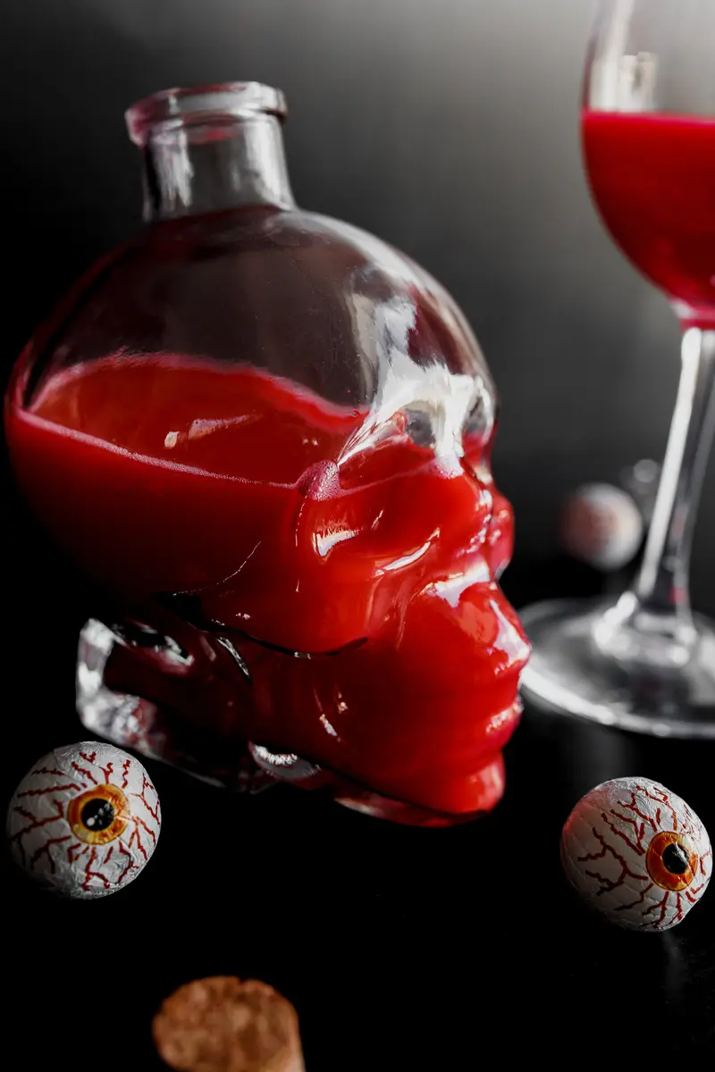 Red drink in a skull shaped decanter, on a table with chocolates that look like eyes.