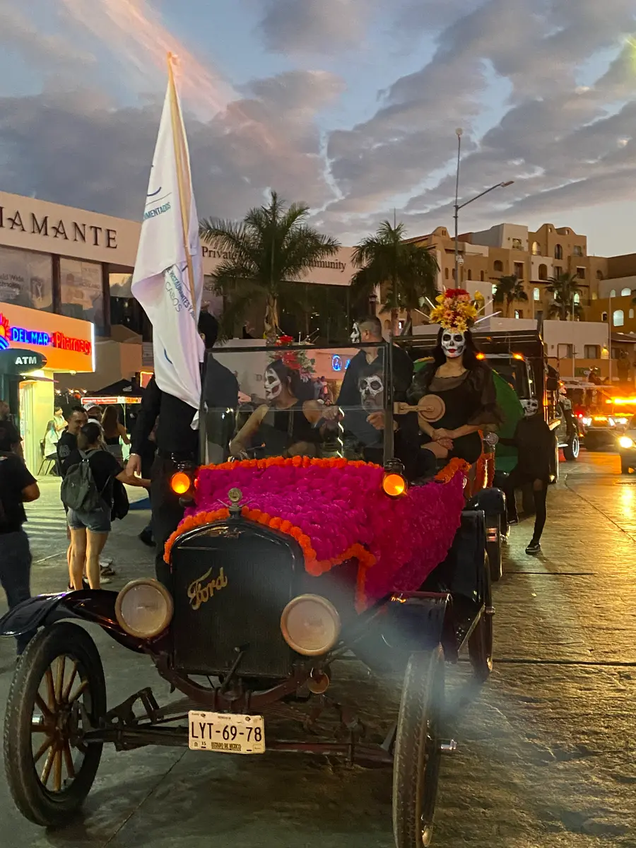 Antique Ford car decorated in colorful Marigold flowers with people dressed as catrinas and skelletons riding for Cabos first annual Day of the Dead parade. 