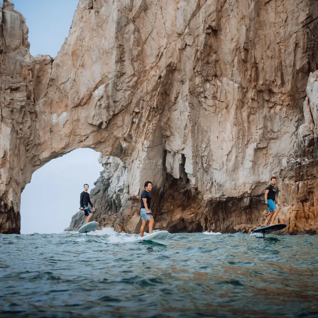 Three men riding electric surf boards in front of El Arco in Cabo, Mexico. 