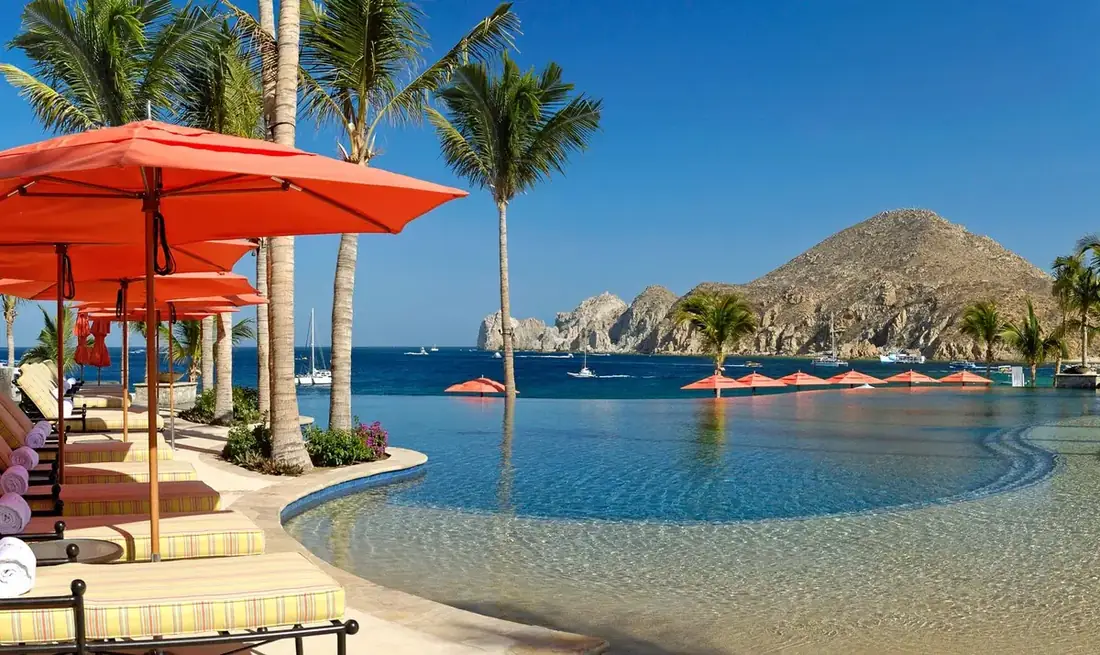 Infinity pool fading into the beach, hills in the background, lounge chairs and parasols lining the pool.