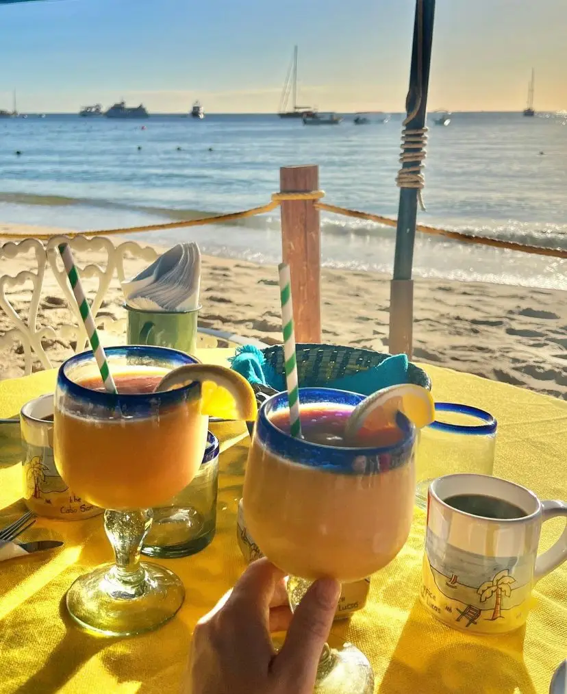 Two people toasting at The Office on Medano Beach with the waves crashing on the sand in the background. 