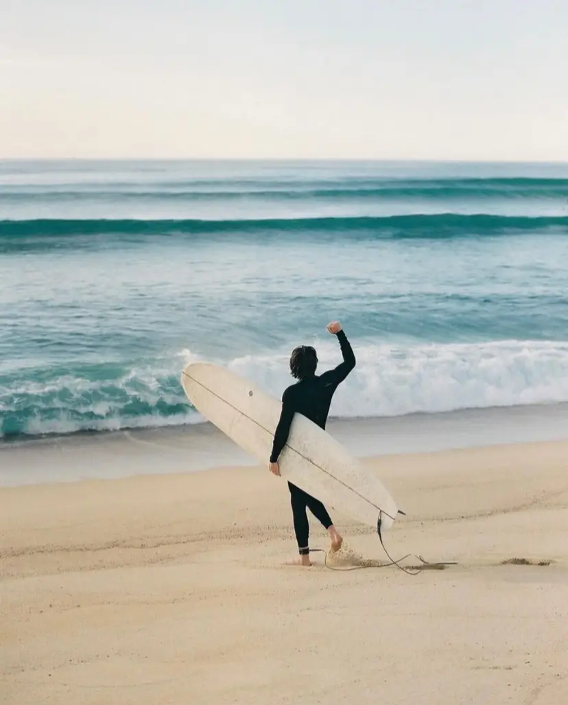 Man ina wetsuit with a board under his arm walking towards the waters of La Fortuna