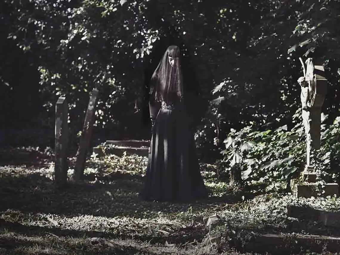 Woman in black standing ominously in a graveyard. 