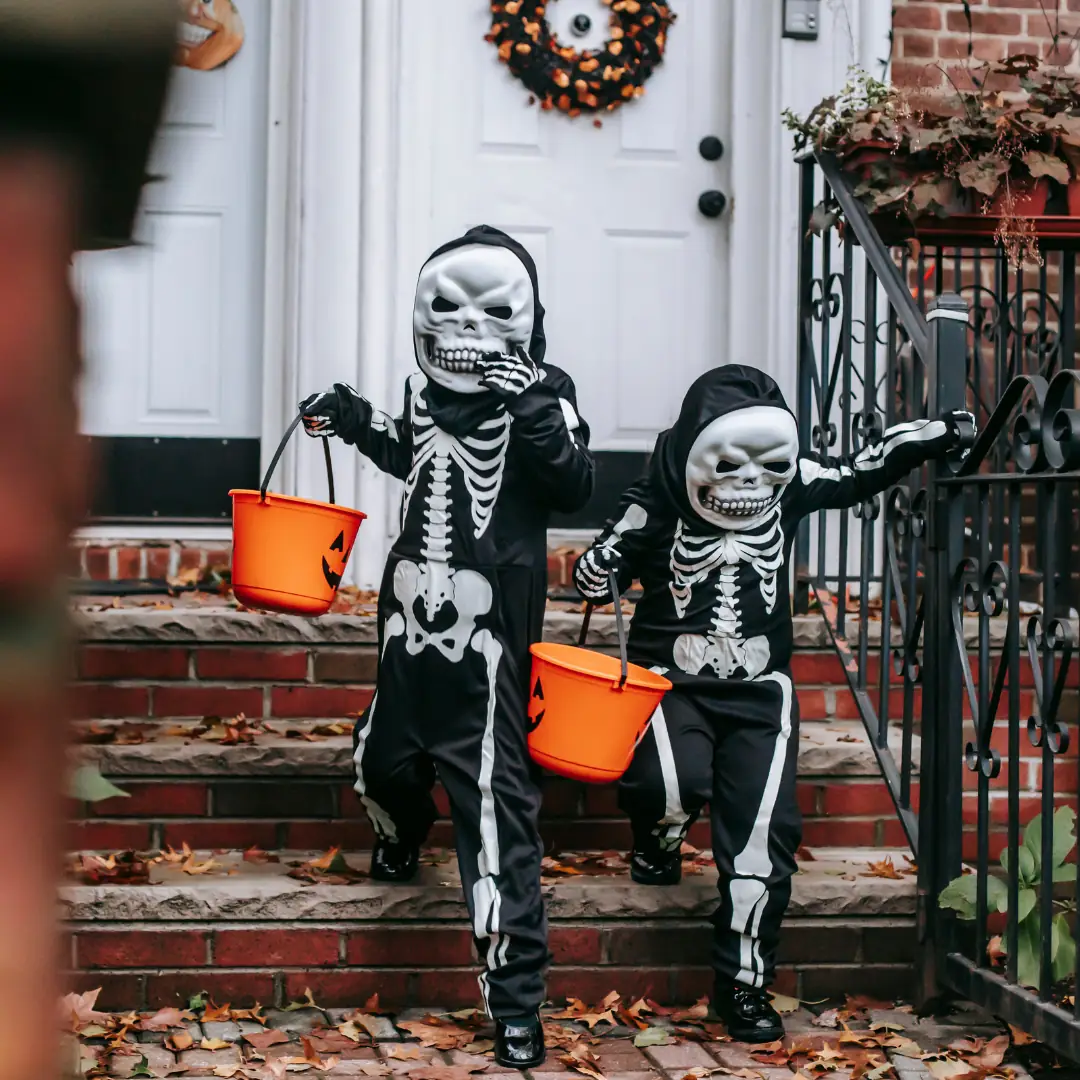 Two small kids dressed up as skeletons, wearing masks, trick or treating. 