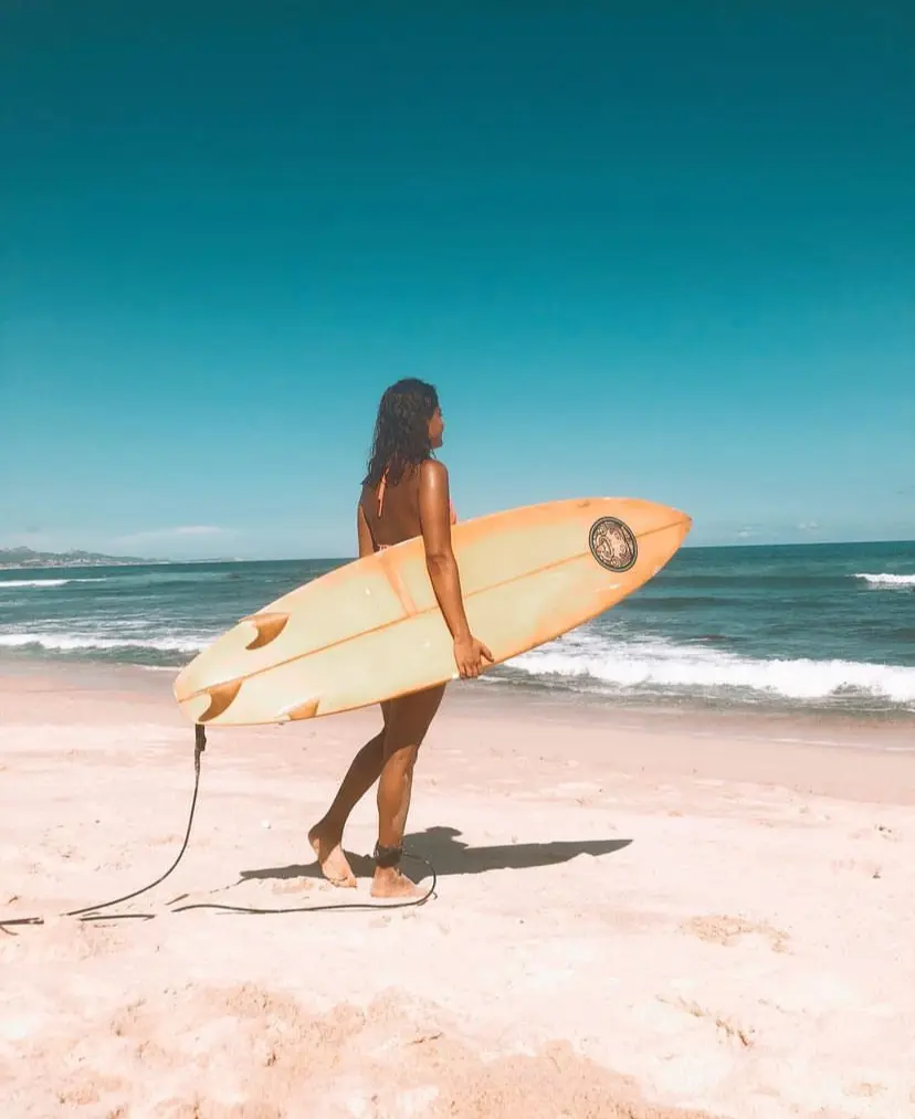 Woman holding a surf board under her arn as she walks towards the waters of Costa Azul in Mexico. 