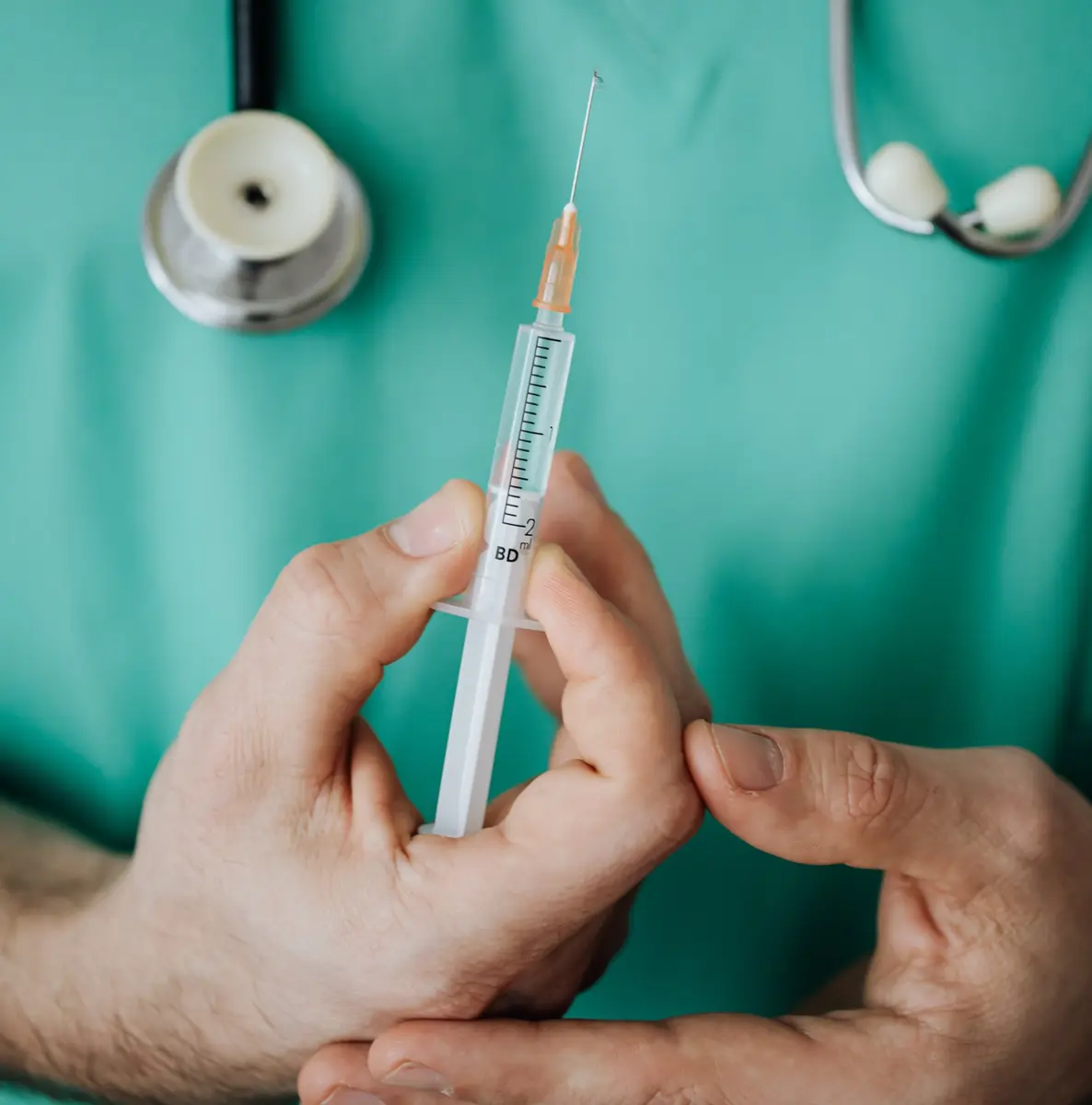 Person in scrubs wearing a stethoscope, holding an injection