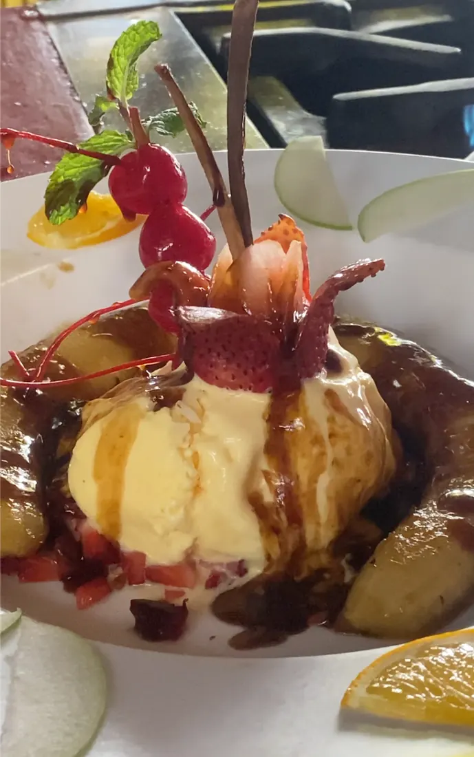 Bananas Flambé from El Squid Roe in Cabo Mexico- scoop of vanilla ice cream surrounded by a banana halved longways and flambes, covered in caramel drizzle, topped with cherries.