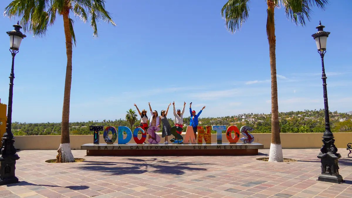 Group of friends posing with the Letters of Todos Santos on a bright, sunny day in Mexico.