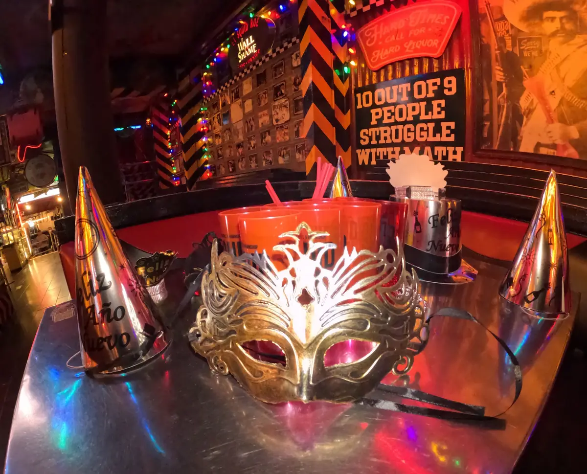 Golden mask resting on a table in El Squid Roe in Cabo San Lucas, Mexico; surrounded by hats, glasses, and decorations for New Year's Eve.