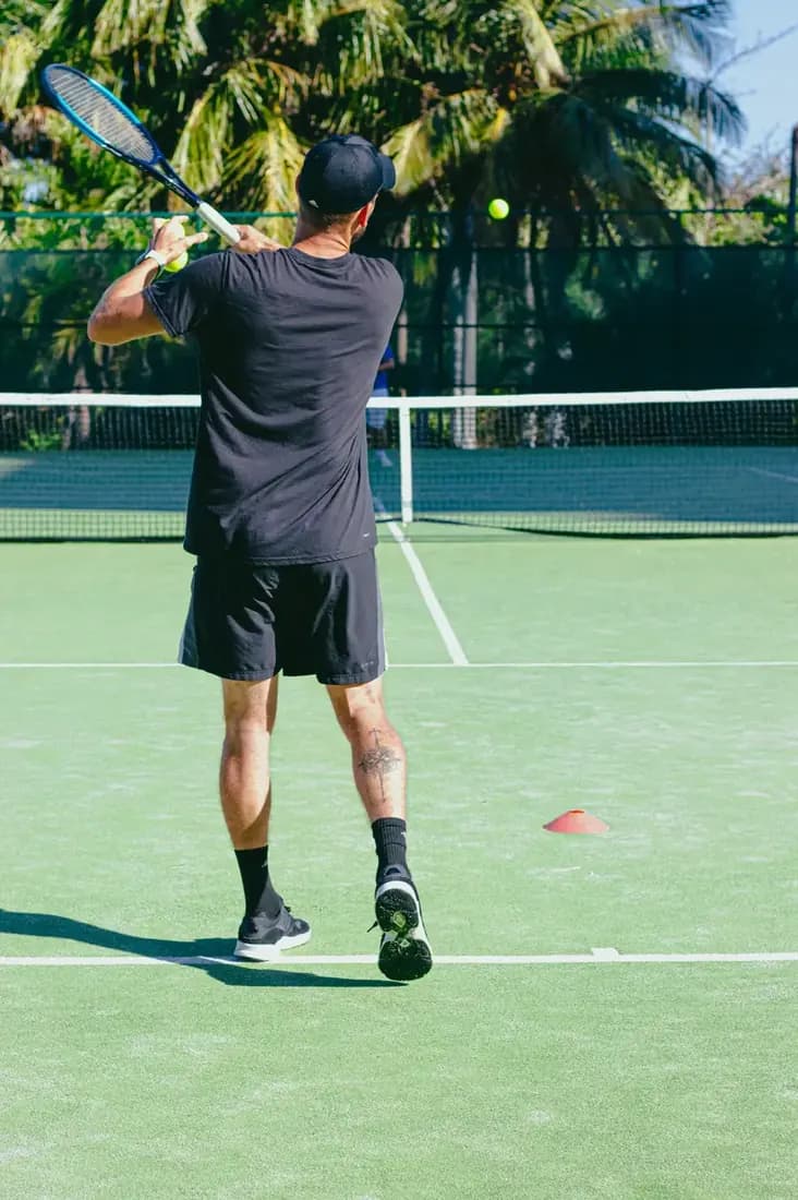 Person about to hit the tennis ball, shot from behind.