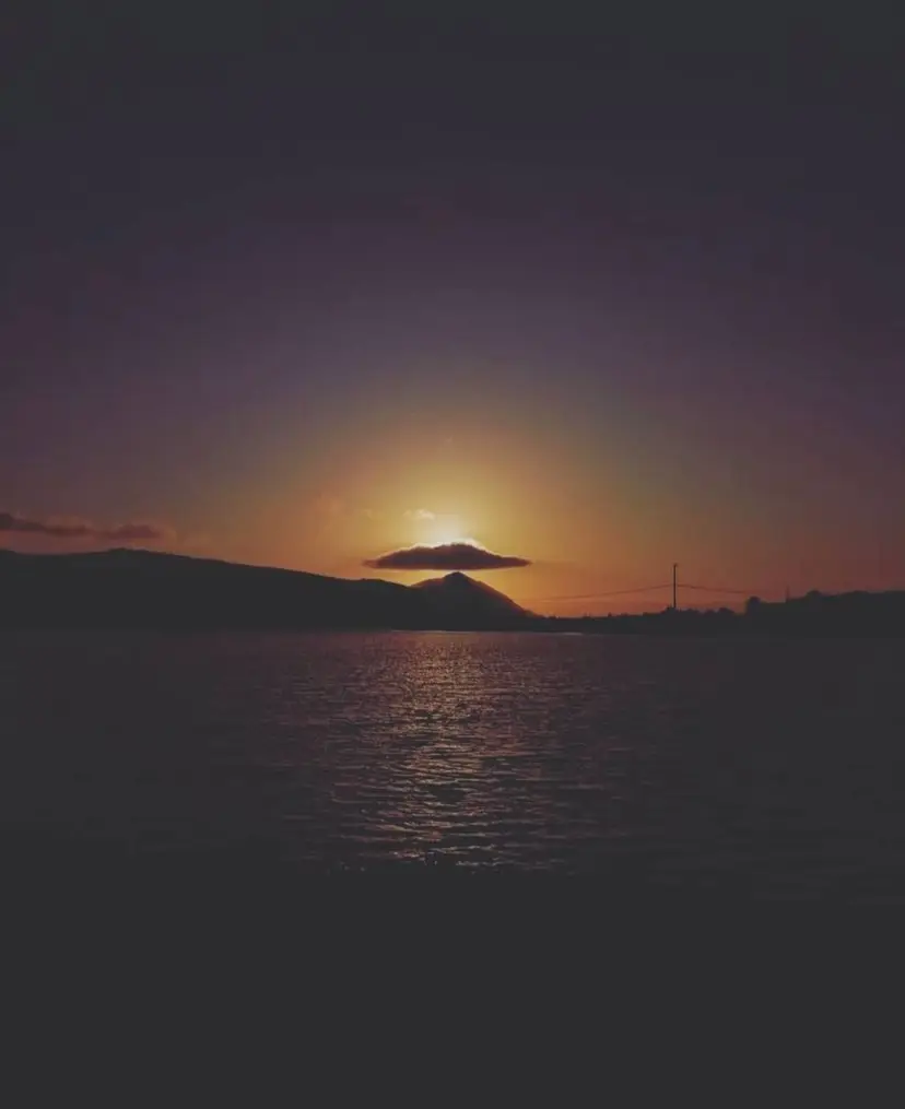 Sunset seen from the water at La Bufadora, right behind a hill with a cloud right over it.