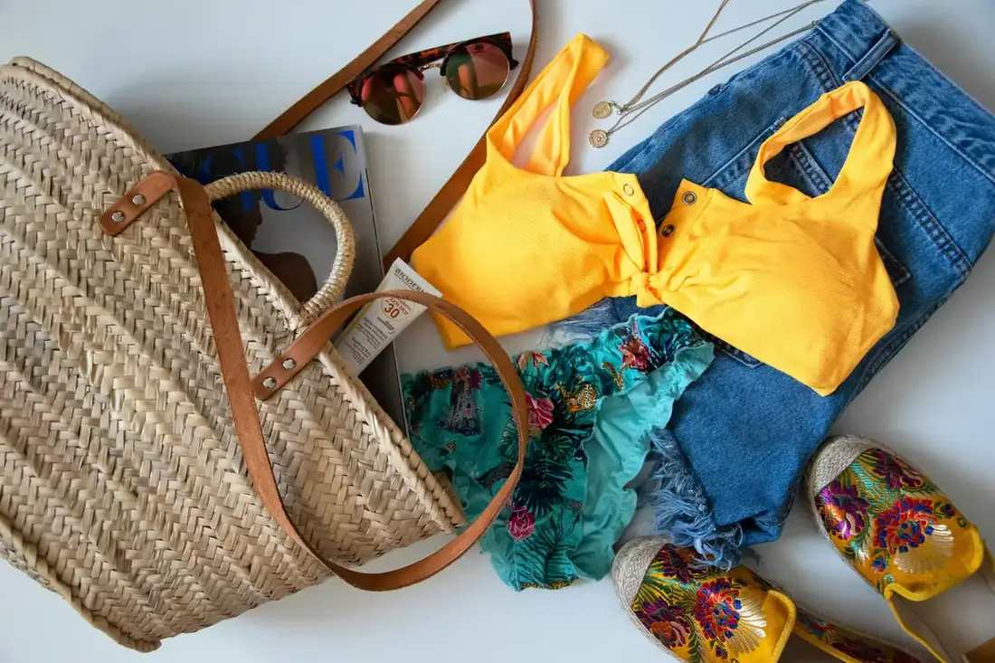 Beach bag with jean shorts, colorful bikini, sunglasses, and a magazine.