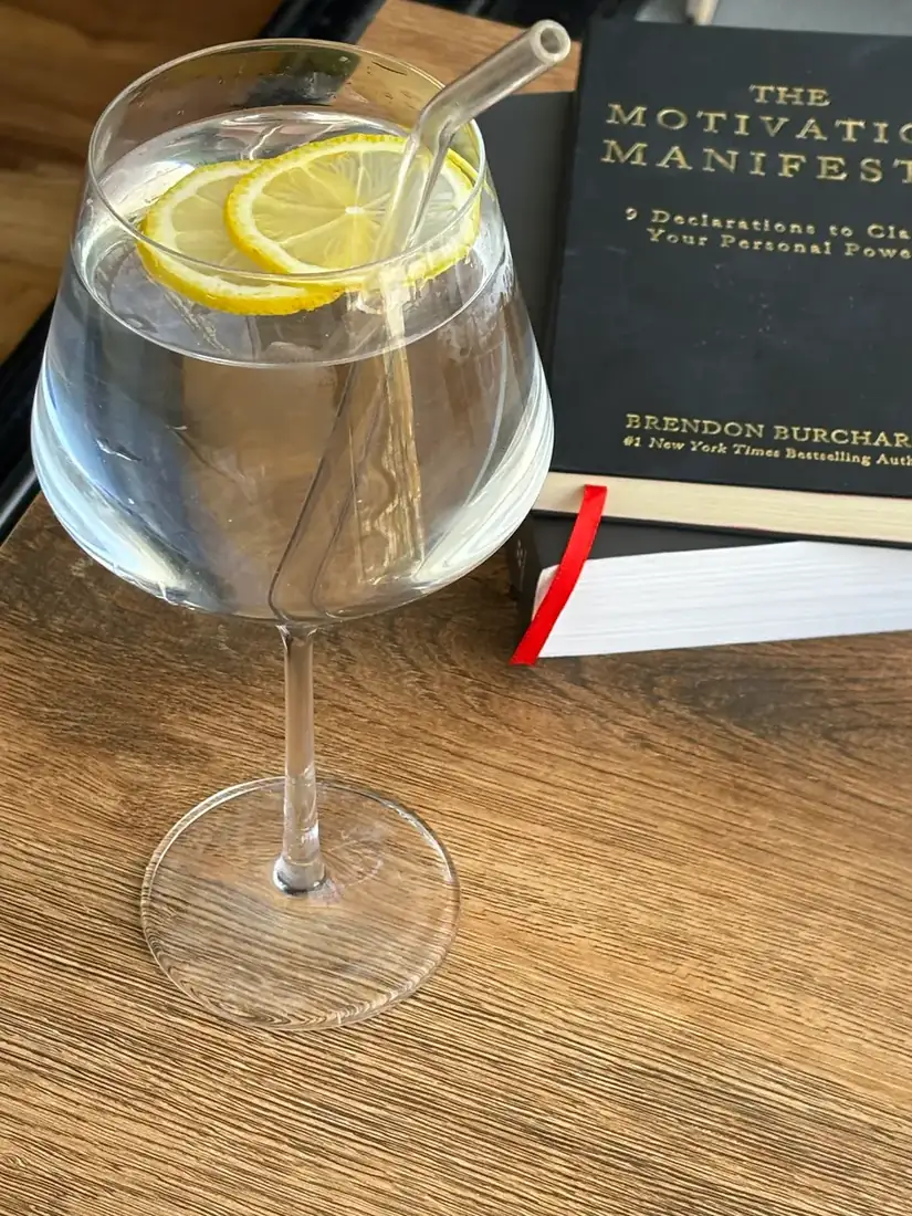 Wine glass filled with water and a couple of lemon slices with a glass straw, and a pair of books stacked behind it.