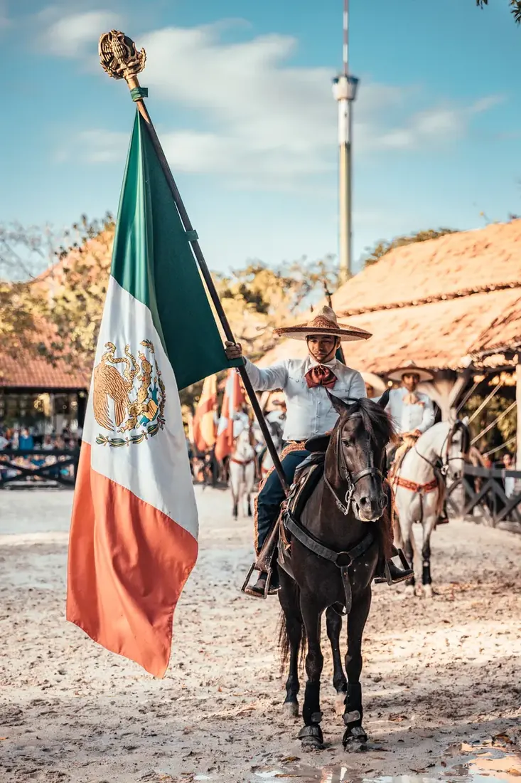 Man riding horse holding a huge Mexican flag.