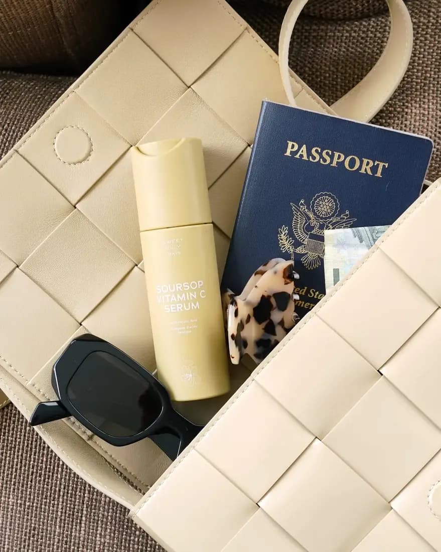 Purse with glasses, passport, hair clip, and vitamin c serum.