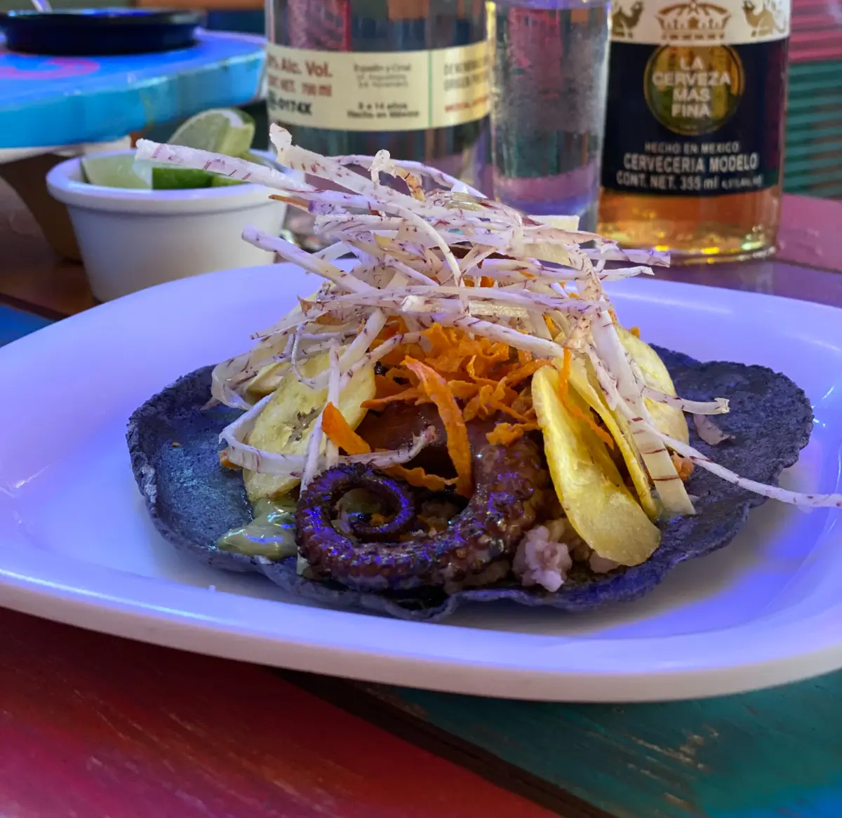 Grilled octopus taco topped with crisps, served with a beer.