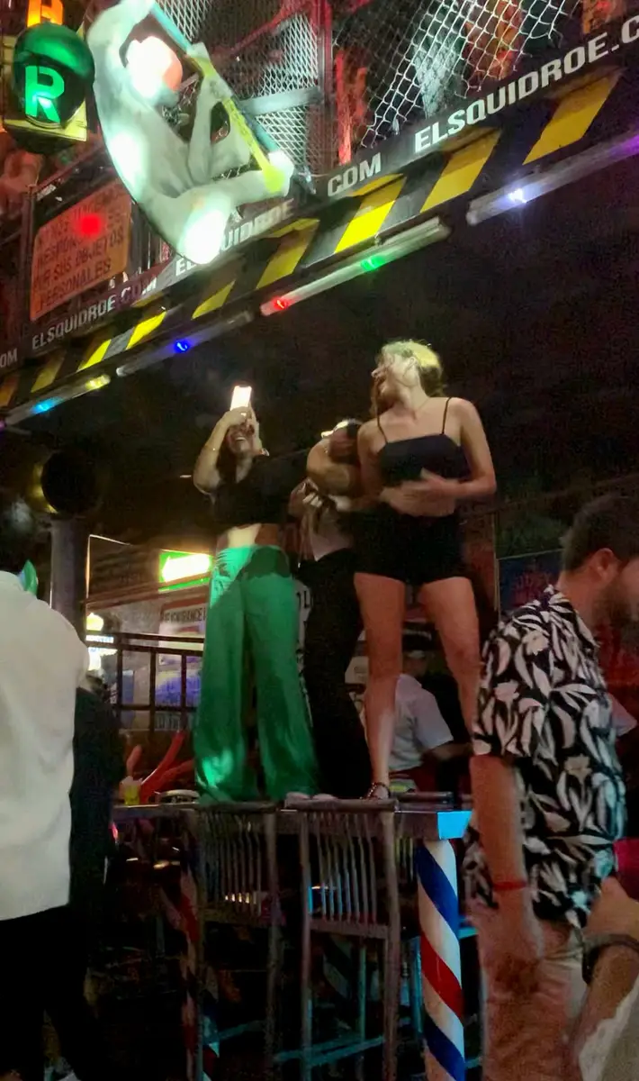 Three women dancing on top of a table at El Squid Roe in Cabo, Mexico.