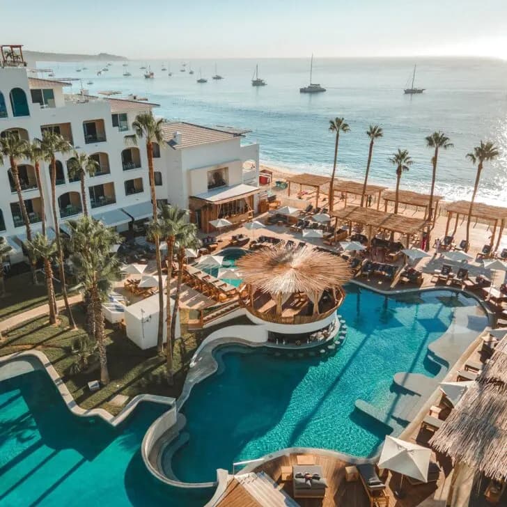 Pool at ME Cabo seen from above with the DJ booth in the center and Medano Beach in the background.
