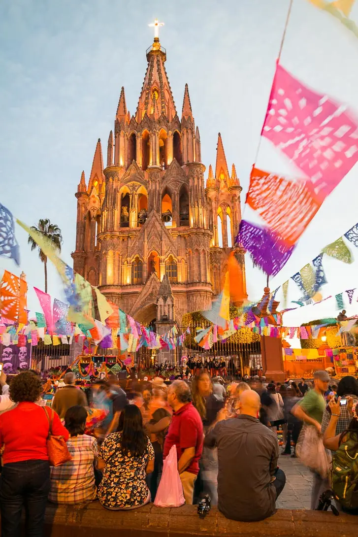 Crowd gathered in front of the Parroquia of San Miguel, with colorful papel picado over them.