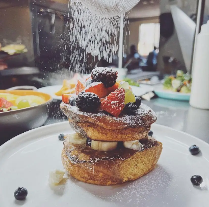 Stacked French Toast, with fruit in between toasts, and topping it, glass sugar being sprinkled on top.