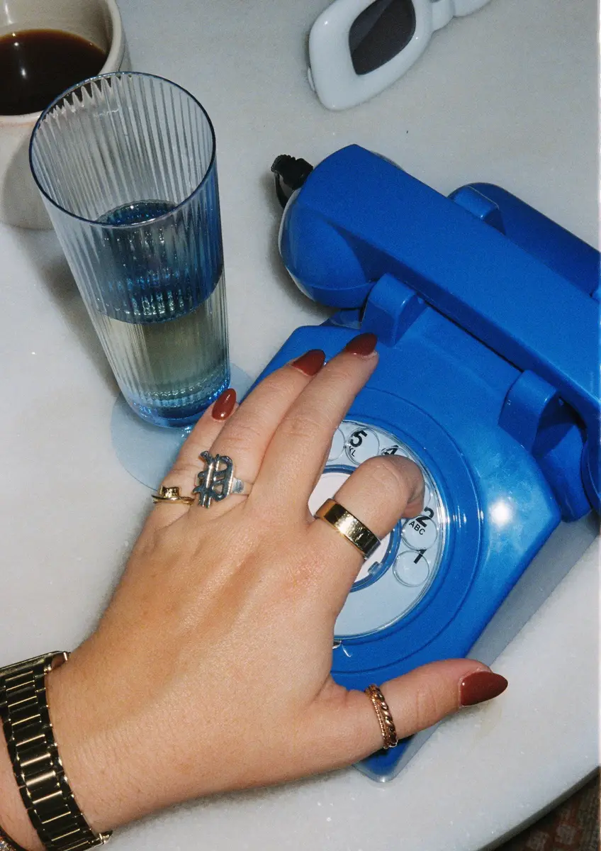 Hand dialing on a rotary phone with a cup of coffee and sunglasses in the background.