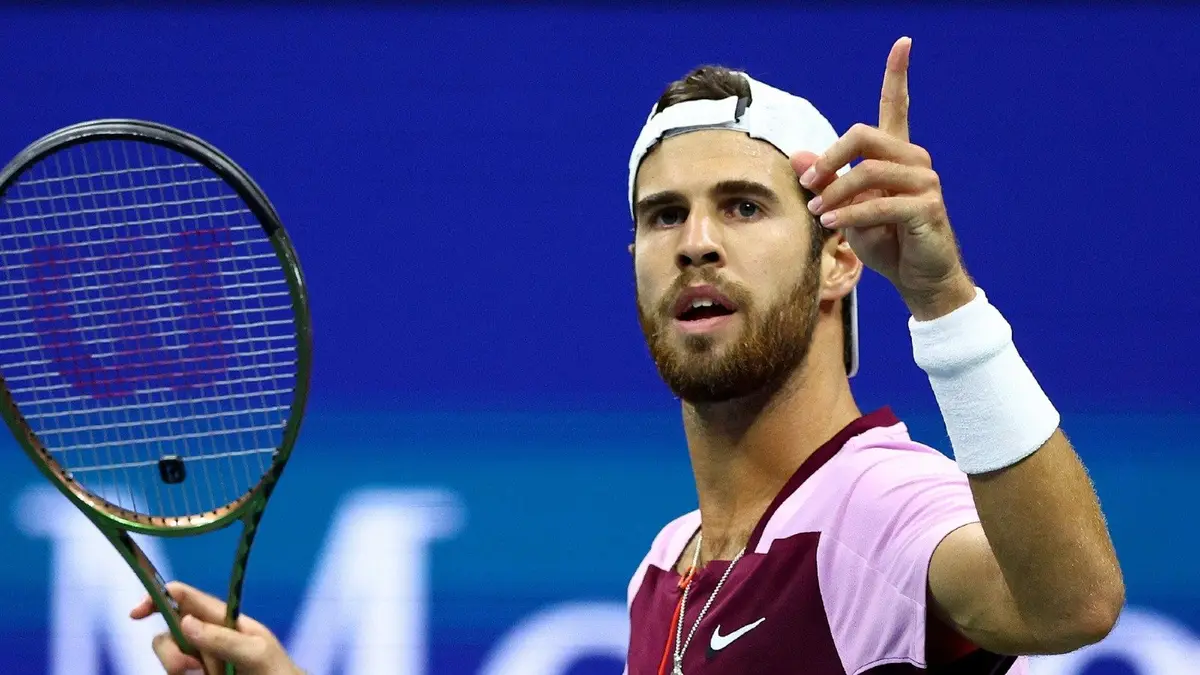 Karen Khachanov pointing his finger in the air with his tennis racket in the other hand.