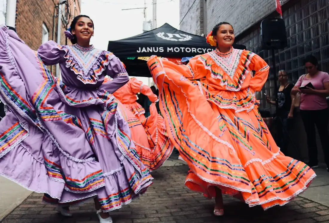 Two women in traditional Mexican dresses dancing in a 5 de Mayo parade.
