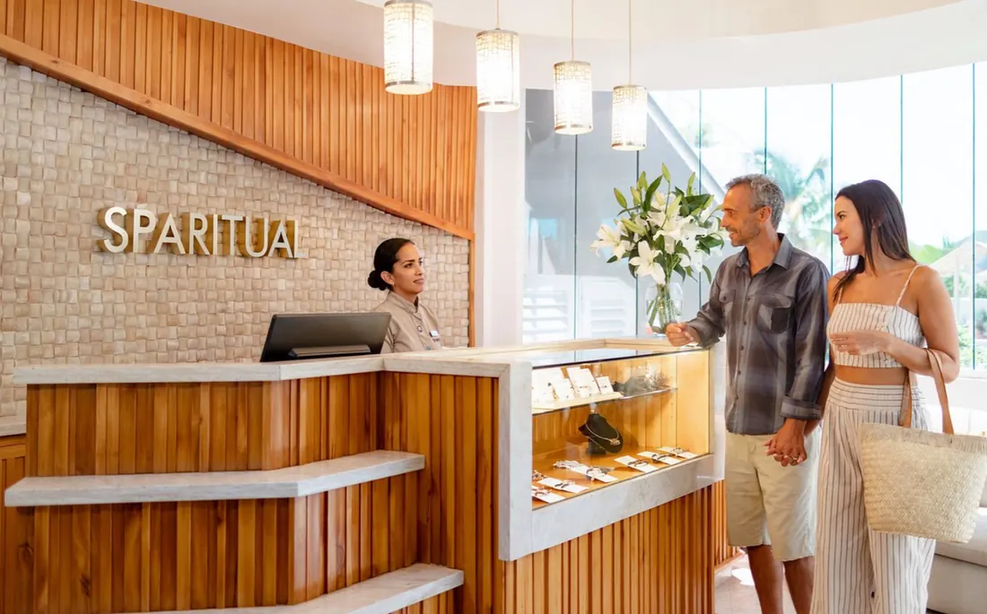 A couple holding hands, arriving to the lobby of Sparitual, where they are greeted by a receptionist.