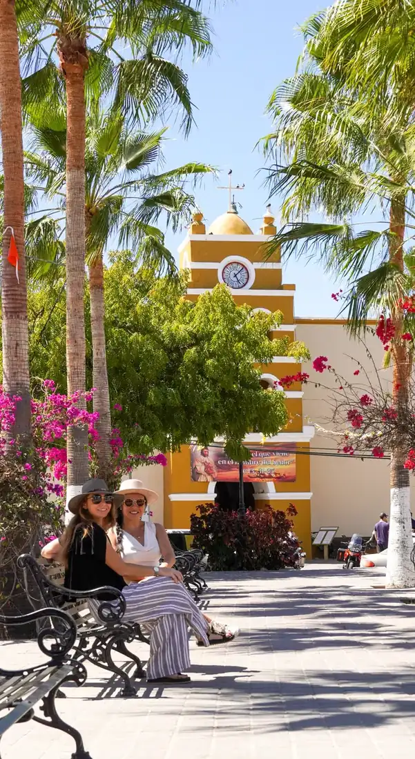 Two women sitting on a bench in front of the church of Todos Santos, Mexico.