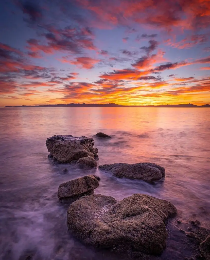 Sun setting on the Bay of Loreto, with small waves crashing on rocks close to the shore.