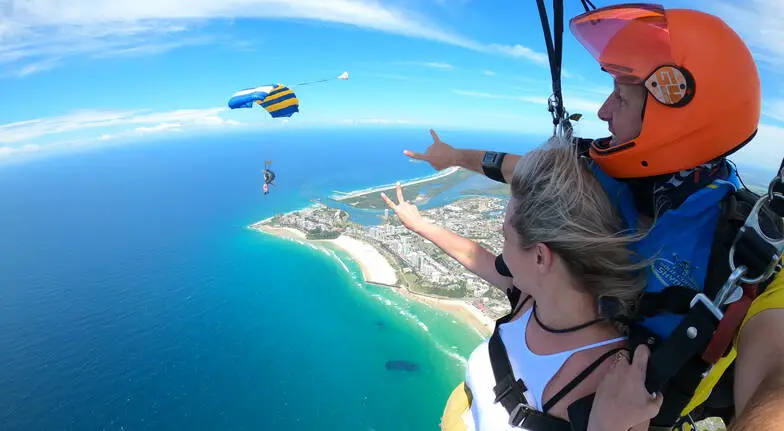 Woman with her guide peacing out fellow skydivers with Cabo beneath them.