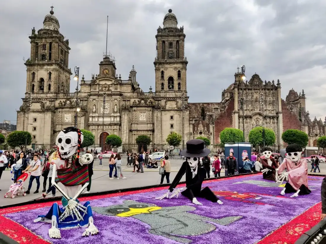 Display of large scale skeletons, sitting over arrangements made with flowers, all in front of a church in Mexico City.