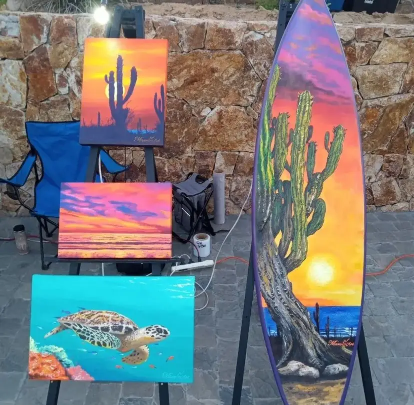 Multiple paintings of Baja scenes, like a cactus at sunset, a turtle swimming under water, and more at the Art Walk of Cabo, Mexico.