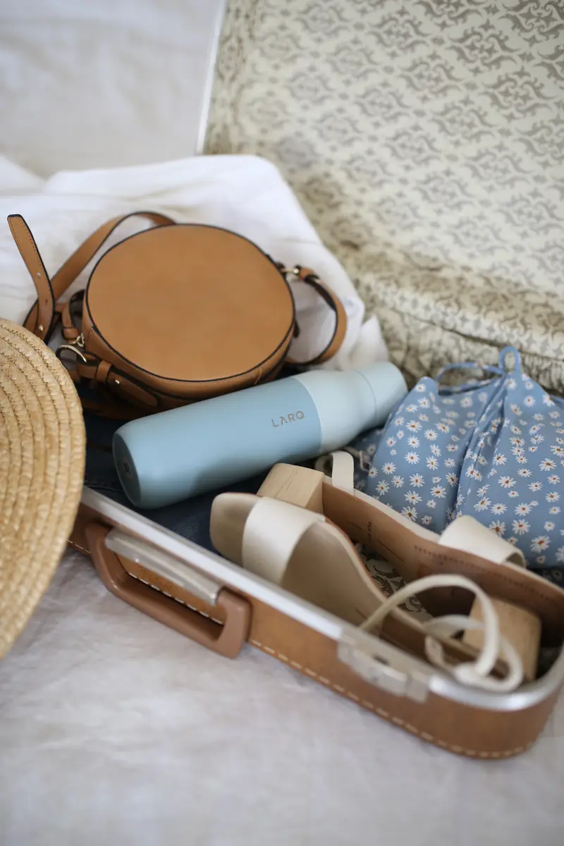 Lugage with sandals, purse, reusable water bottle and clothes.