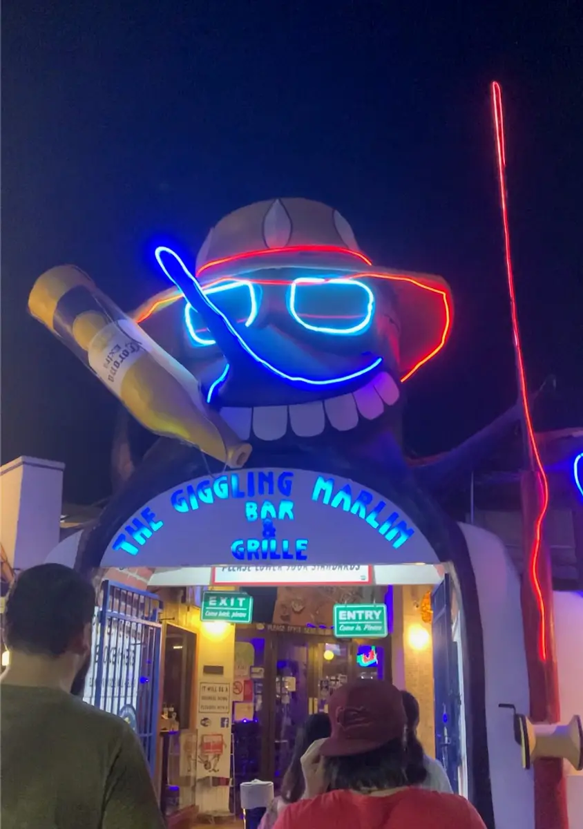 Group of people entering Giggling Marlin. The entrance illuminated by colorful neon lights.
