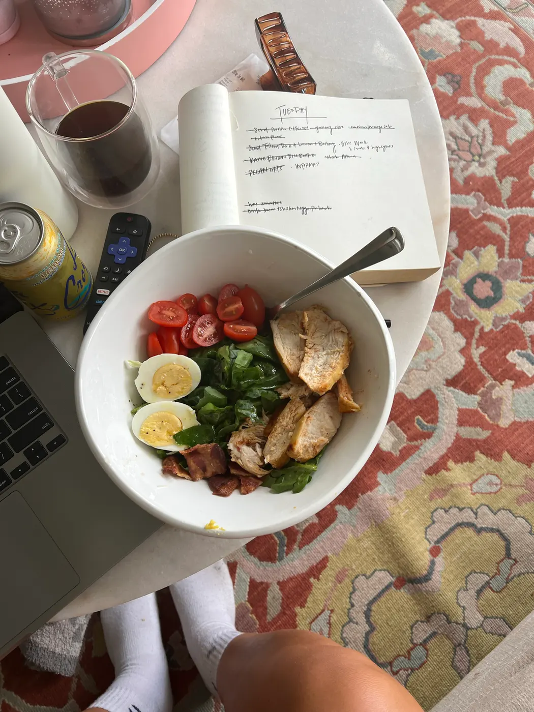 Bowl of salad on a table next to a notebook with writing in it.