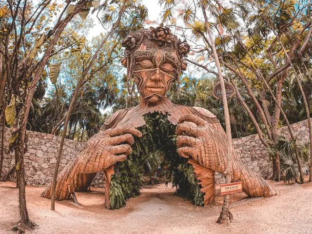 Wooden statue of a person from the chest up, holing its chest open, while looking down. The inside of the chest is filled with greenery.